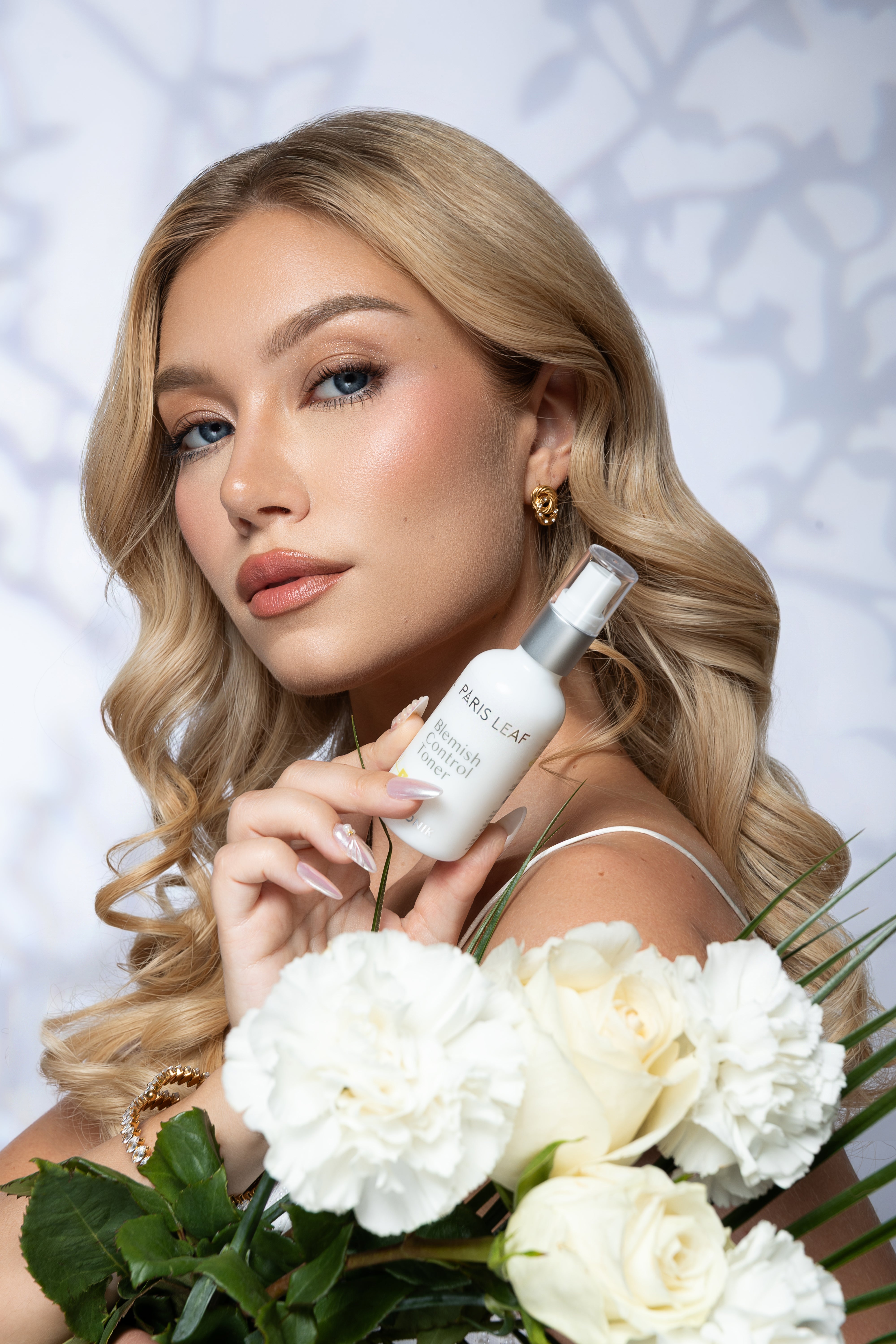 Miss Universe Hungary holding Parisleaf Blemish Control Toner beside a bouquet of white flowers.