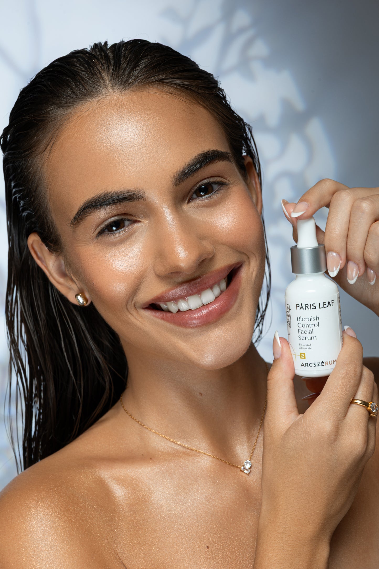 Smiling woman holding a bottle of Parisleaf Blemish Control Facial Serum.