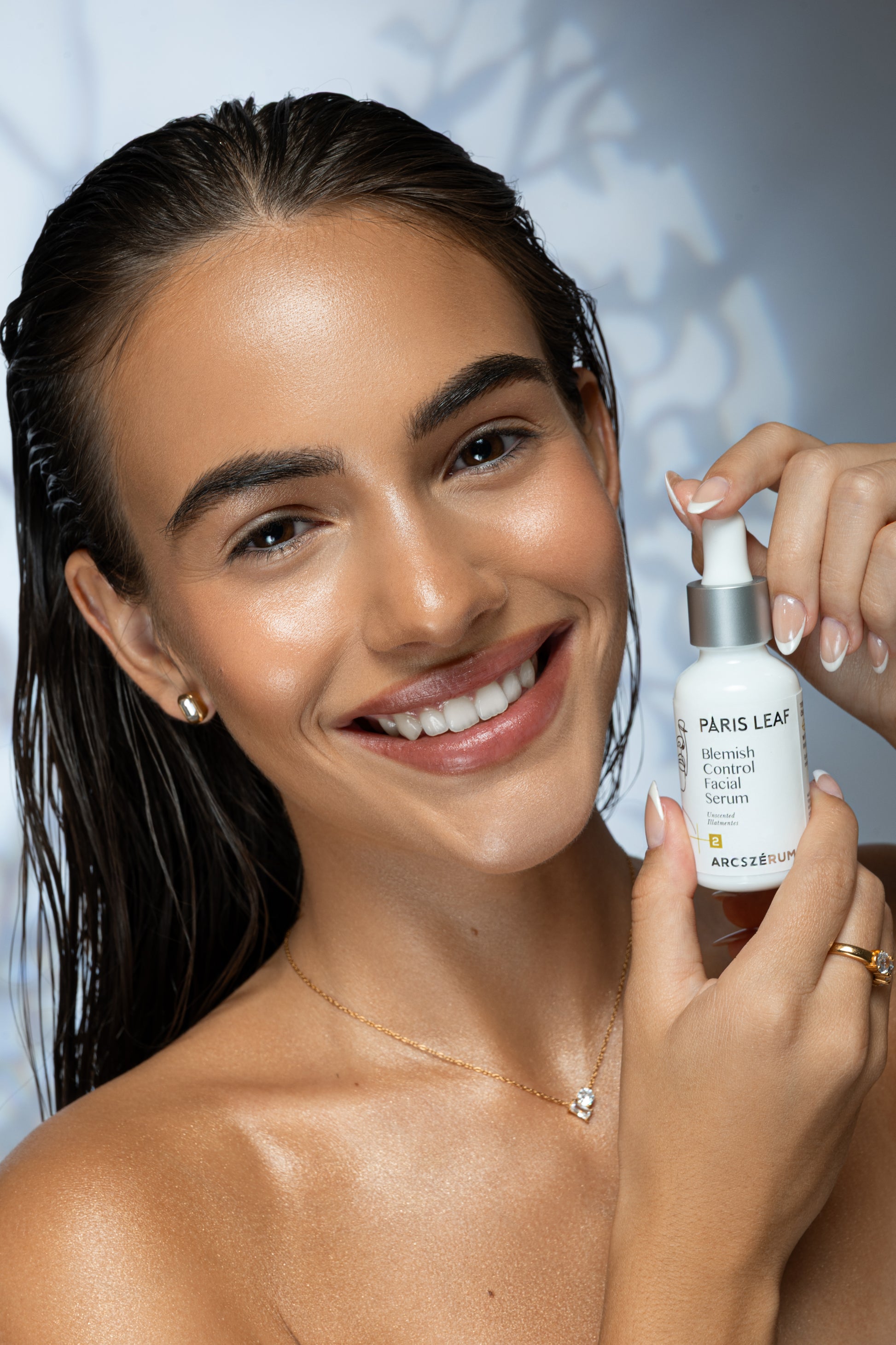 Smiling woman holding a bottle of Parisleaf Blemish Control Facial Serum.