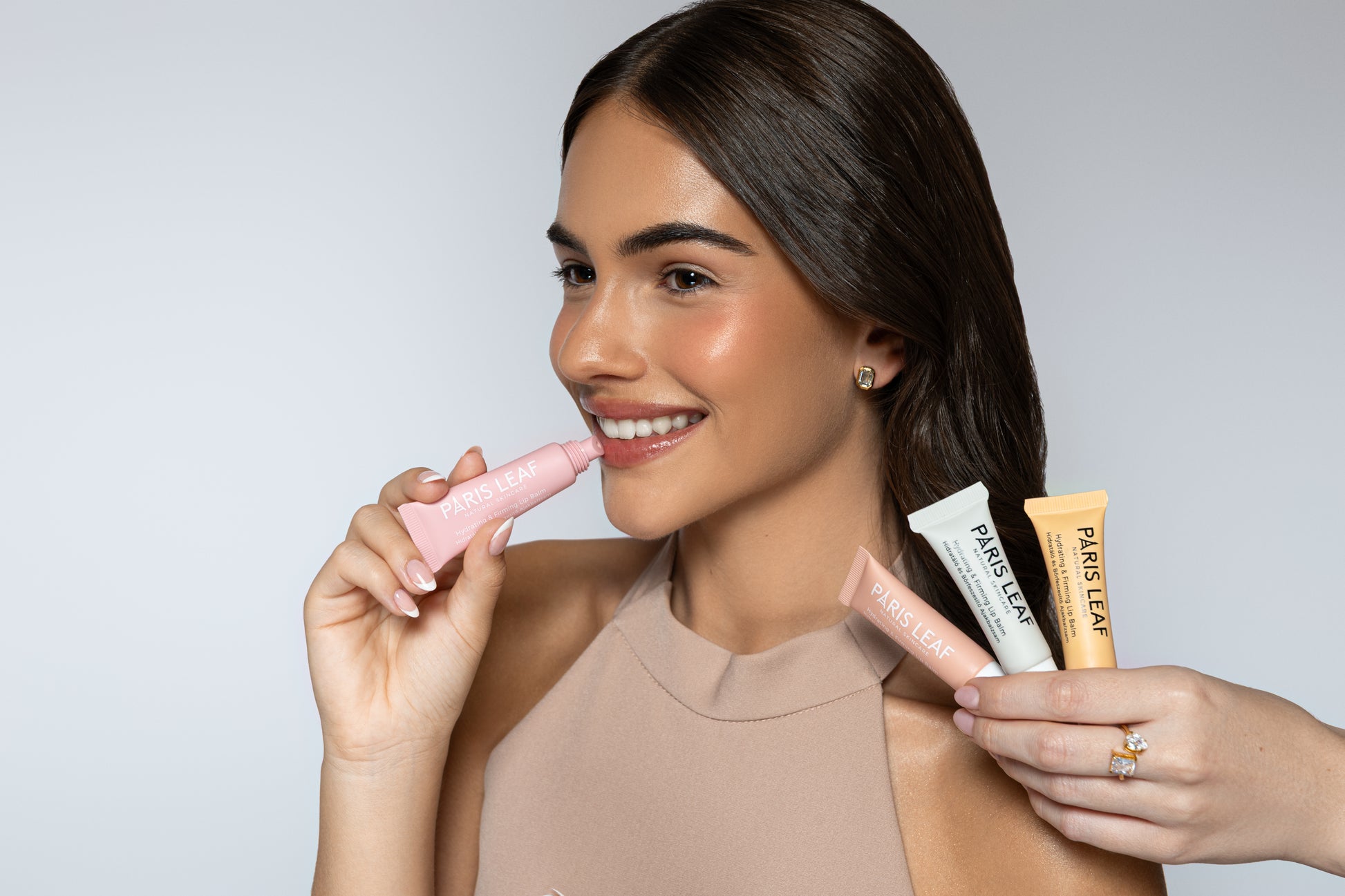 Smiling woman applying Parisleaf Hydrating & Firming Lip Balm while holding three other lip balms.