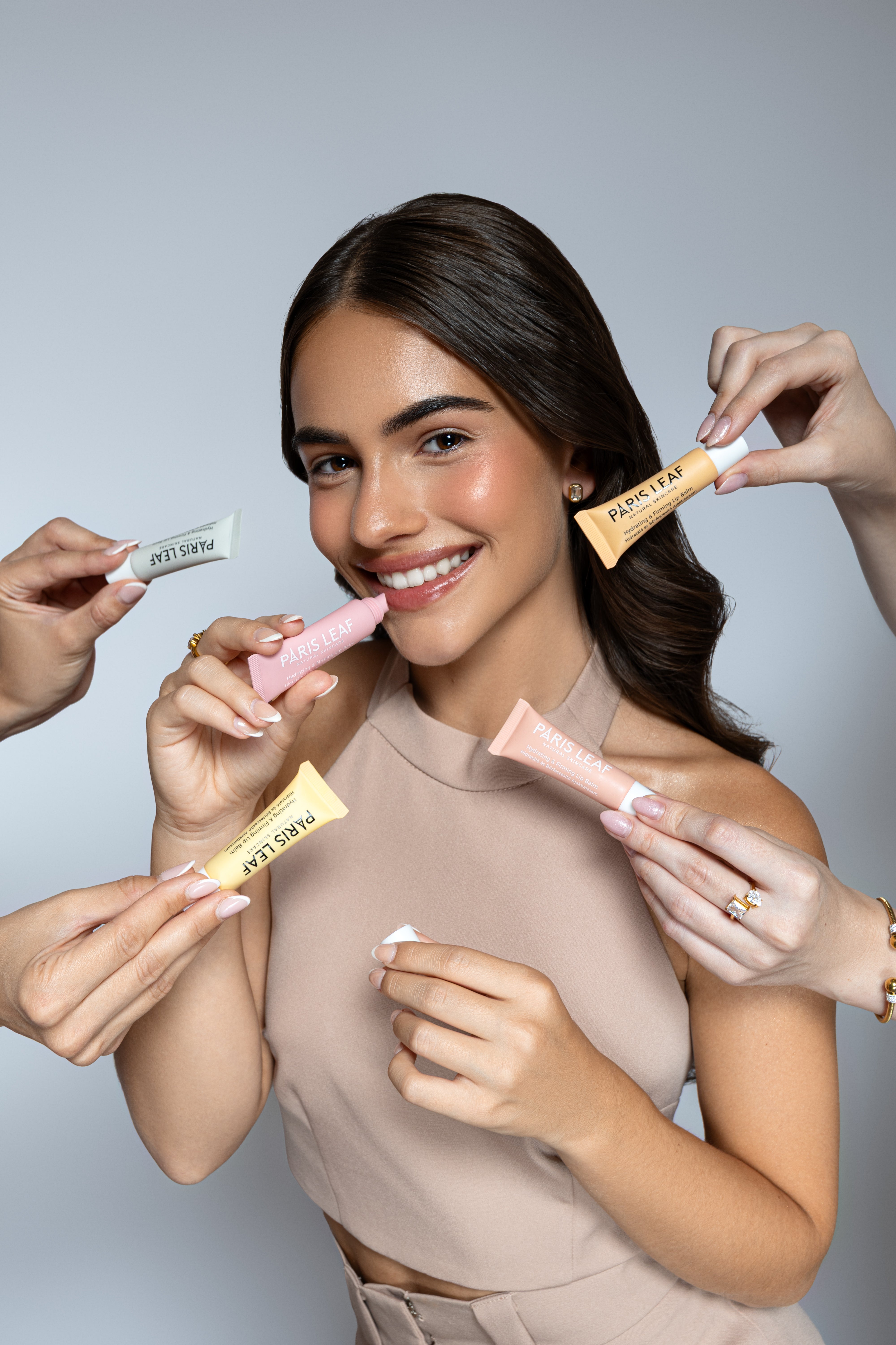 Smiling woman holding a Parisleaf lip care product while hands display the colorful lip balm collection.